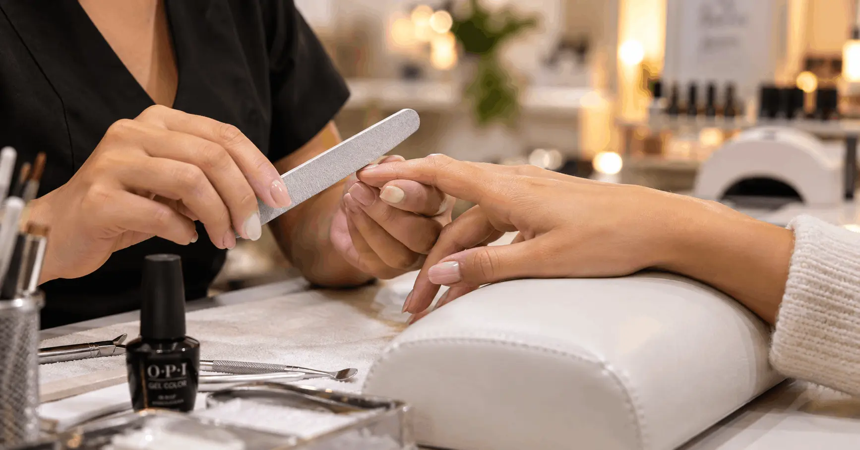 Nail technician filing a client's nails at a salon station